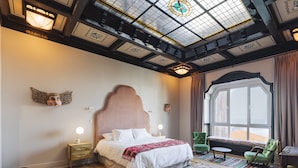 A bedroom with a large bed, a wooden floor, a skylight, a window with curtains, and a green chair. - Casablu Hotel (Valparaiso)