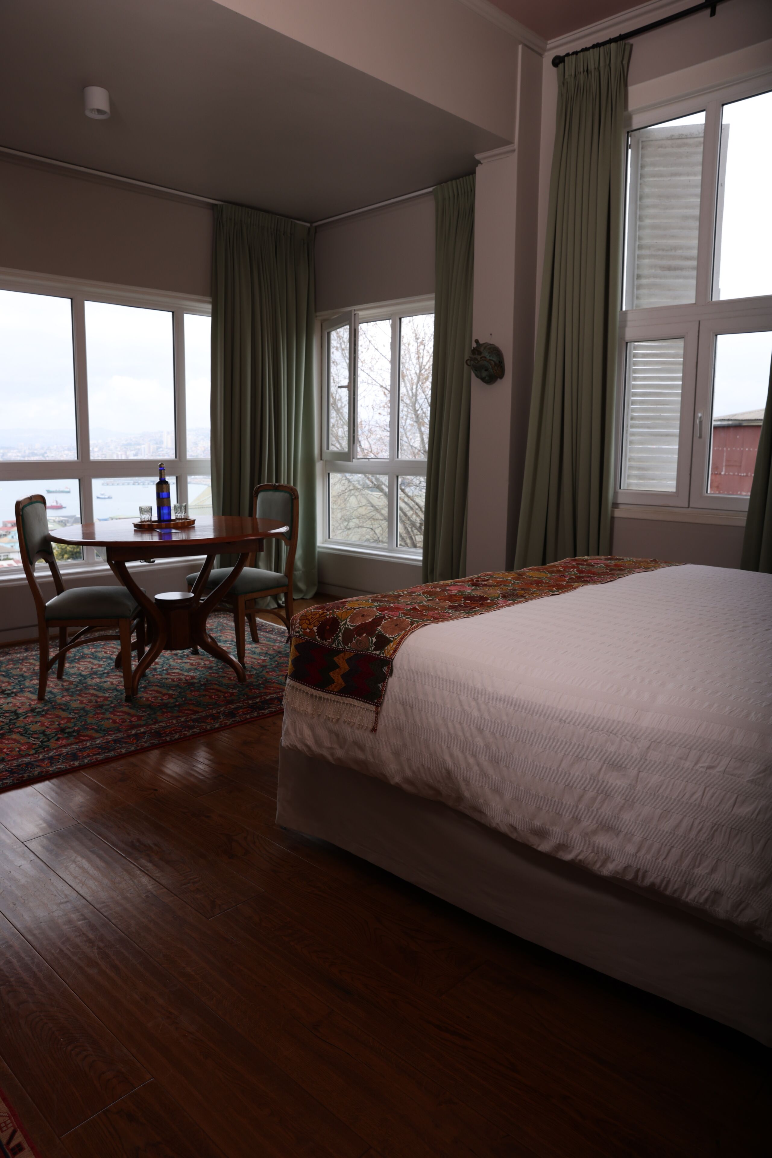 A bedroom with a bed, a table with chairs, and large windows.