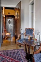 Una habitación con puerta de madera, un sillón tapizado en azul, una mesita redonda y una alfombra estampada.