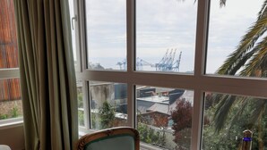 A room with a large window, a round table with a bottle and glasses, a chair, and a curtain. - Casablu Hotel (Valparaiso)