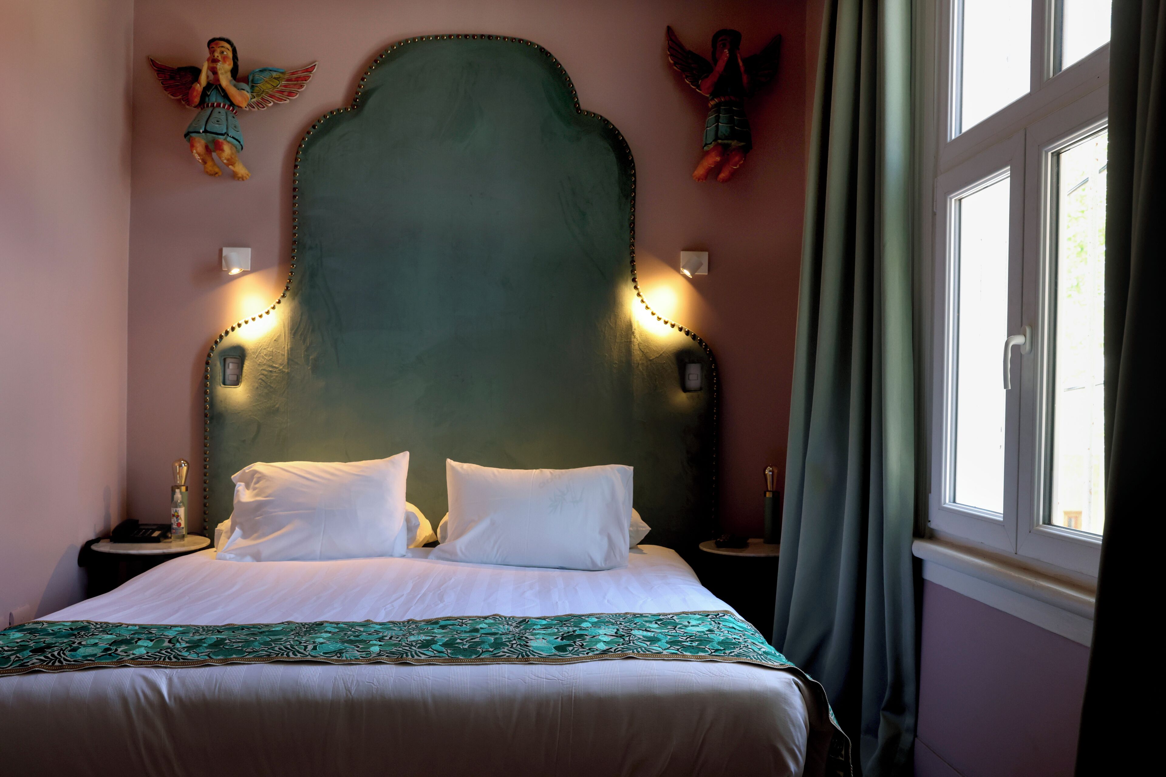 Una cama con ropa de cama blanca, un cabecero verde y figuras decorativas de ángeles en la pared.