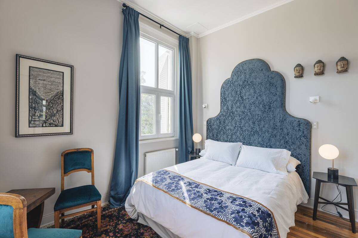 Un dormitorio con una cama, una silla, una mesa y una ventana con cortinas.