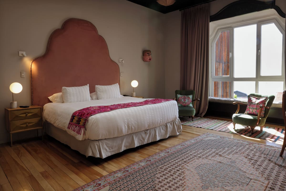 Un dormitorio con una cama grande, lámparas de noche, una silla y una ventana con cortinas.