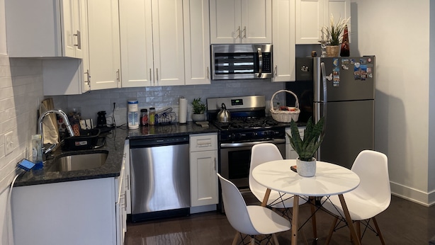 A modern kitchen with white cabinets, stainless steel appliances, a dishwasher, and a dining area with a table and chairs.