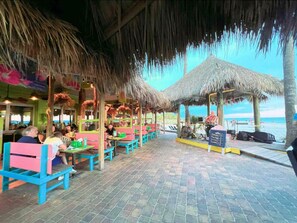 An outdoor restaurant with thatched roofs, colorful seating, and a view of the sea. - The happy family Hideaway (Port Charlotte)
