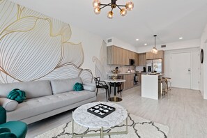 Uma sala de estar moderna com um sofá, uma mesa de centro e uma cozinha ao fundo.