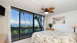 Een slaapkamer met een grote schuifpui die leidt naar een balkon met uitzicht op het strand en de oceaan.