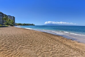 A beach with clear blue water, a sandy shore, and a distant mountain.