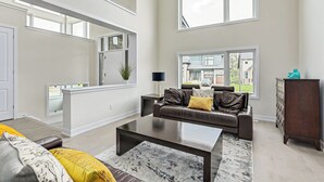 Ein geräumiges Wohnzimmer mit hoher Decke, einem modernen Kamin und großen Fenstern mit Blick ins Freie.