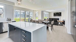 Eine moderne Küche mit einer großen Kochinsel, Essbereich mit Stühlen, einem an der Wand montierten Fernseher und einem Balkon mit Blick auf Häuser.