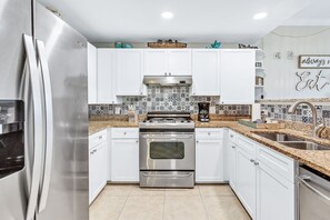 Features a double oven, refrigerator, and sink, with stainless steel appliances and a patterned tile backsplash.