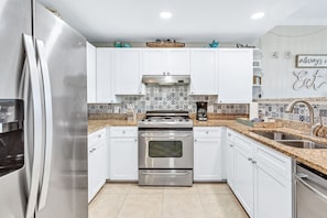 Features a double oven, refrigerator, and sink, with stainless steel appliances and a patterned tile backsplash.