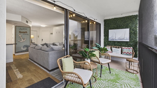 Een gezellige zithoek met een grijze bank, rieten fauteuils en een vloerkleed met groene patronen.