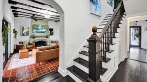Ein modernes Wohnzimmer mit Kamin, Treppe und Fernseher, der eine Poolszene zeigt.