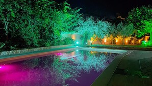 Ein beleuchteter Poolbereich bei Nacht, mit Bäumen, die sanft leuchten, und einem Pool, der die Lichter spiegelt.