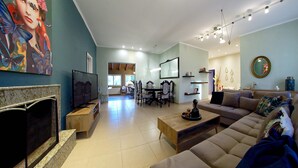 Ein geräumiges Wohnzimmer mit großem Fernseher, Kamin, einer Couch und einem Essbereich im Hintergrund.