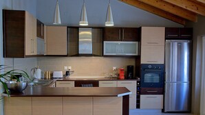 Eine moderne Küche mit Holzbalkendecke, Edelstahlgeräten und Pendelleuchten.