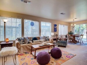 A spacious living room with a sofa, ottomans, a coffee table, and a dining area with chairs and a table.