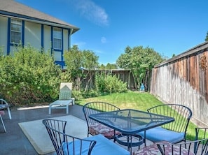 A backyard with a patio area featuring a metal table and chairs, a small bench, and a wooden fence.