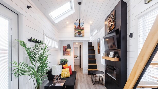 Ein modernes Interieur mit einem schwarzen Sofa, einem Esstisch, einem Blumentopf und einer Treppe, die in eine obere Ebene führt.