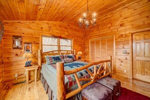 A log cabin bedroom with a wooden bed, a chandelier, and a large window. - Resting Bear Retreat Hot Tub Pool Table Fire Pit (Blue Ridge)