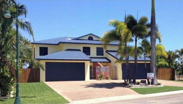 Ein zweistöckiges Haus mit einer dunkelblauen Garage, einem Vorgarten mit Palmen und einem strahlend blauen Himmel.