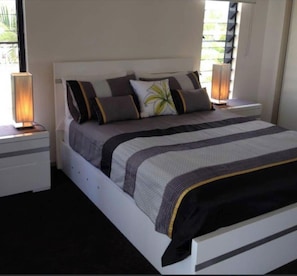 Restful retreat with a neatly made bed, bedside table, and window with blinds.