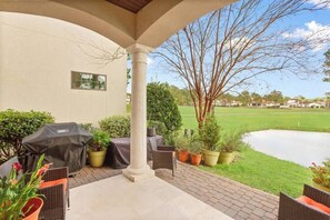 An outdoor patio with a grill, seating, and a view of a golf course and pond.