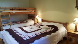 A bunk bed with a white mattress and a quilt, a bedside table with a lamp, and a wooden headboard. - Gite 8 km from the access to Alpe d'Huez large domain (ALLEMOND)