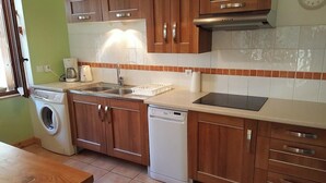 A kitchen with wooden cabinets, a washing machine, a dishwasher, and a countertop with a sink. - Gite 8 km from the access to Alpe d'Huez large domain (ALLEMOND)