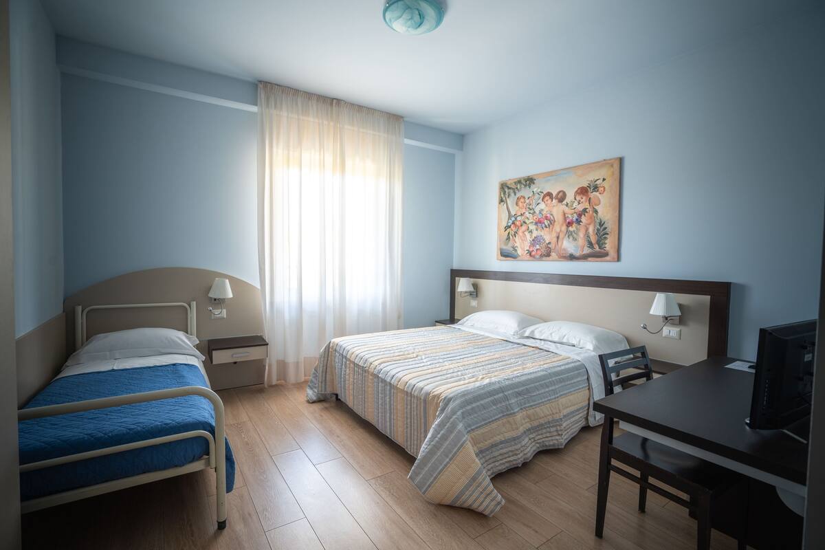 A hotel room with two single beds, a double bed, a desk, and a television.
