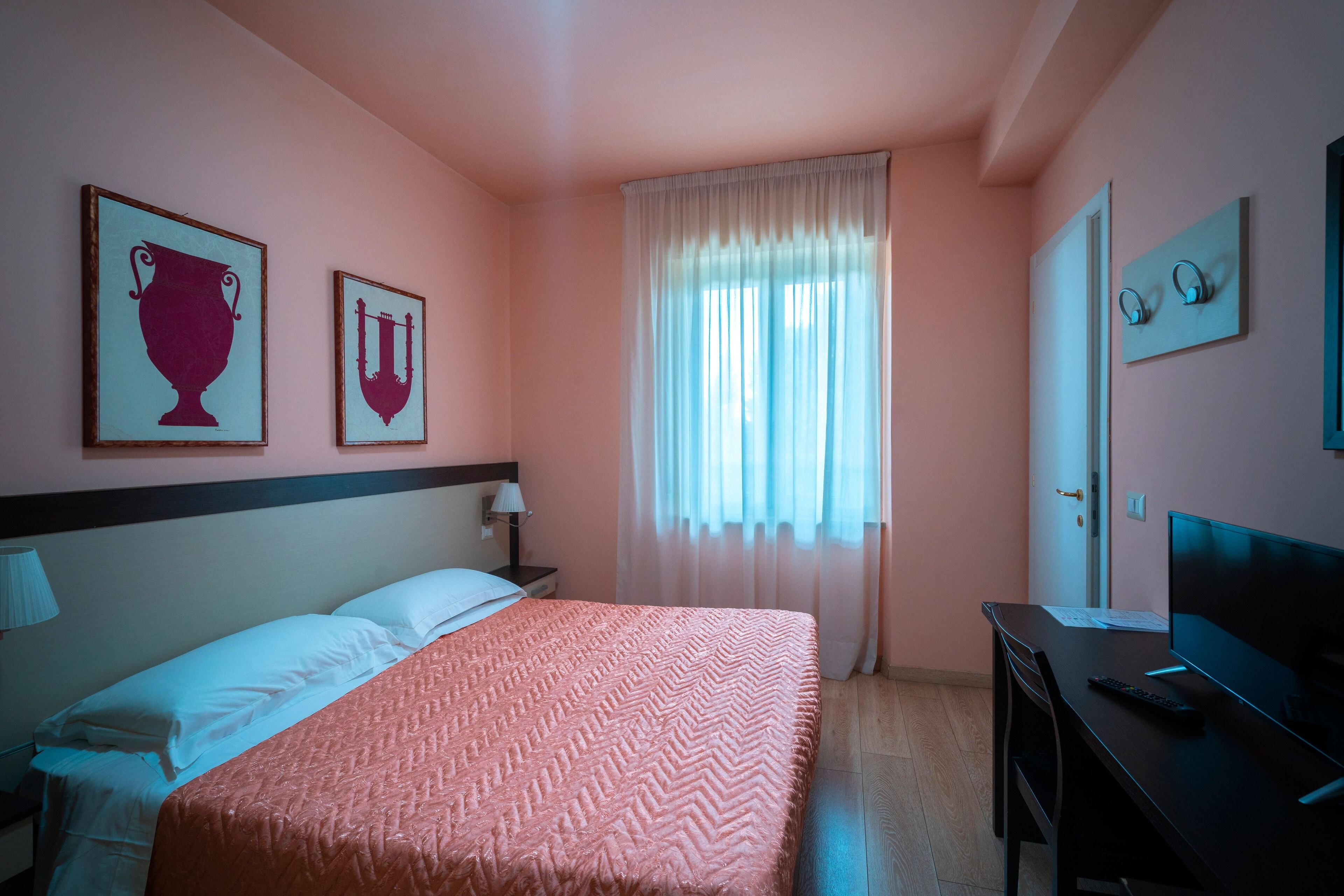 Una habitación de hotel con una cama, un escritorio, un televisor y dos cuadros en la pared.