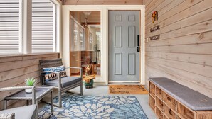 A wooden cabin with a porch, a welcome sign, a bench, and a small table with a plant. - Great Sacandaga Waterfront Retreat (Day)