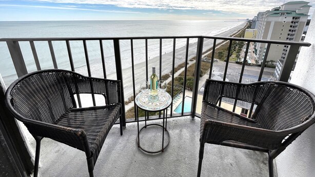 A balcony with two wicker chairs and a small table, overlooking a beach and cityscape. - FANTASTIC OCEAN VIEWS FROM A BEAUTIFUL OCEAN FRONT CONDO! (Myrtle Beach)