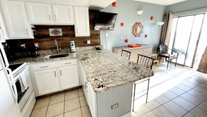 A modern kitchen with white cabinets, granite countertops, and a built-in oven. There is a large window providing natural light and a view of the outdoors. - FANTASTIC OCEAN VIEWS FROM A BEAUTIFUL OCEAN FRONT CONDO! (Myrtle Beach)