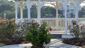 Un pabellón blanco con techo curvo y varias ventanas, rodeado por un jardín con diversas plantas y flores.