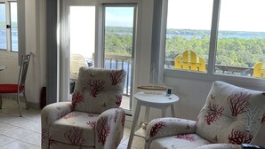 Una habitación con dos sillones reclinables, una mesita redonda y vistas a un lago y un bosque a través de amplios ventanales.