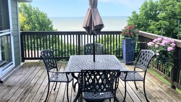 A wooden deck with a table and chairs, an umbrella, and a view of the ocean. - Private Waterfront Loft - an amazing lake view (Leamington)