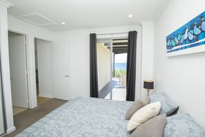 A bedroom with a bed, a painting, and a view of the sea. - Shearwaters Appartment (Penneshaw)