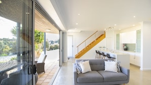 A modern interior with a grey sofa, wooden staircase, and a kitchen with white cabinets. - Shearwaters Appartment (Penneshaw)