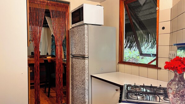 Una cocina con refrigerador, estufa y ventana con vista a follaje.