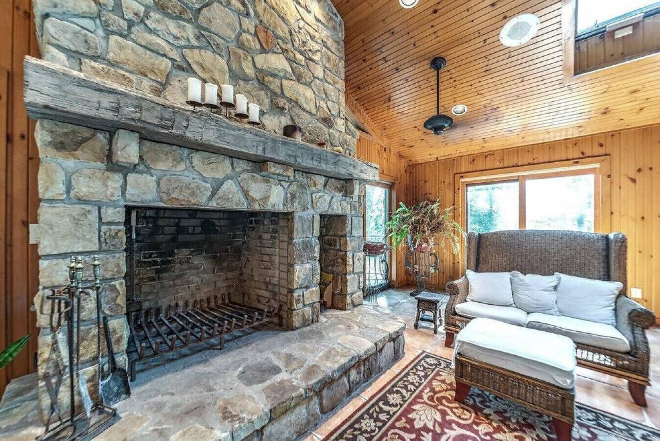 A stone fireplace with a wooden ceiling and a wicker sofa.