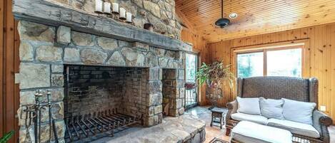 A stone fireplace with a wooden ceiling and a wicker sofa.