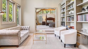 A spacious living room with a large window, a sofa, a coffee table, and a bookshelf.