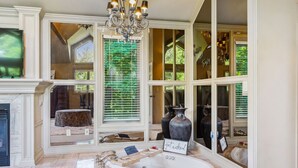 A spacious bathroom with a large bathtub, a chandelier, and a view of the outdoors through large windows.