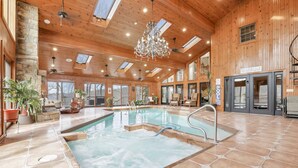 A large indoor swimming pool with a stone floor, wooden walls, and a chandelier.