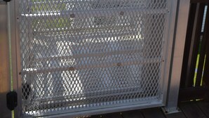 Een overdekt buitengebied met een wit metalen hek en een houten terras.