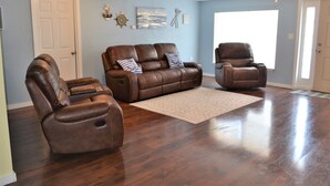 Een woonkamer met een bruine leren bank, twee verstelbare fauteuils en een vloerkleed op een houten vloer.