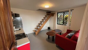 A compact living space with a kitchen, a red sofa, a small table, and a wooden staircase. - Stunning one bed/bath unit. Breathtaking ocean/jungle views with infinity pool! (Quepos)