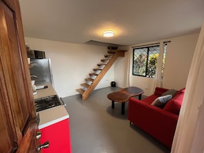 A compact living space with a kitchen, a red sofa, a small table, and a wooden staircase.